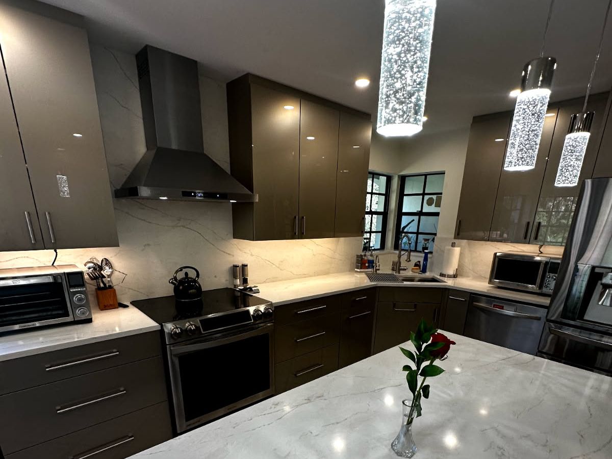 Modern luxury kitchen with high-gloss custom flat-panel cabinetry, a white marble island, and contemporary lighting designed by a premier Sarasota cabinet maker.